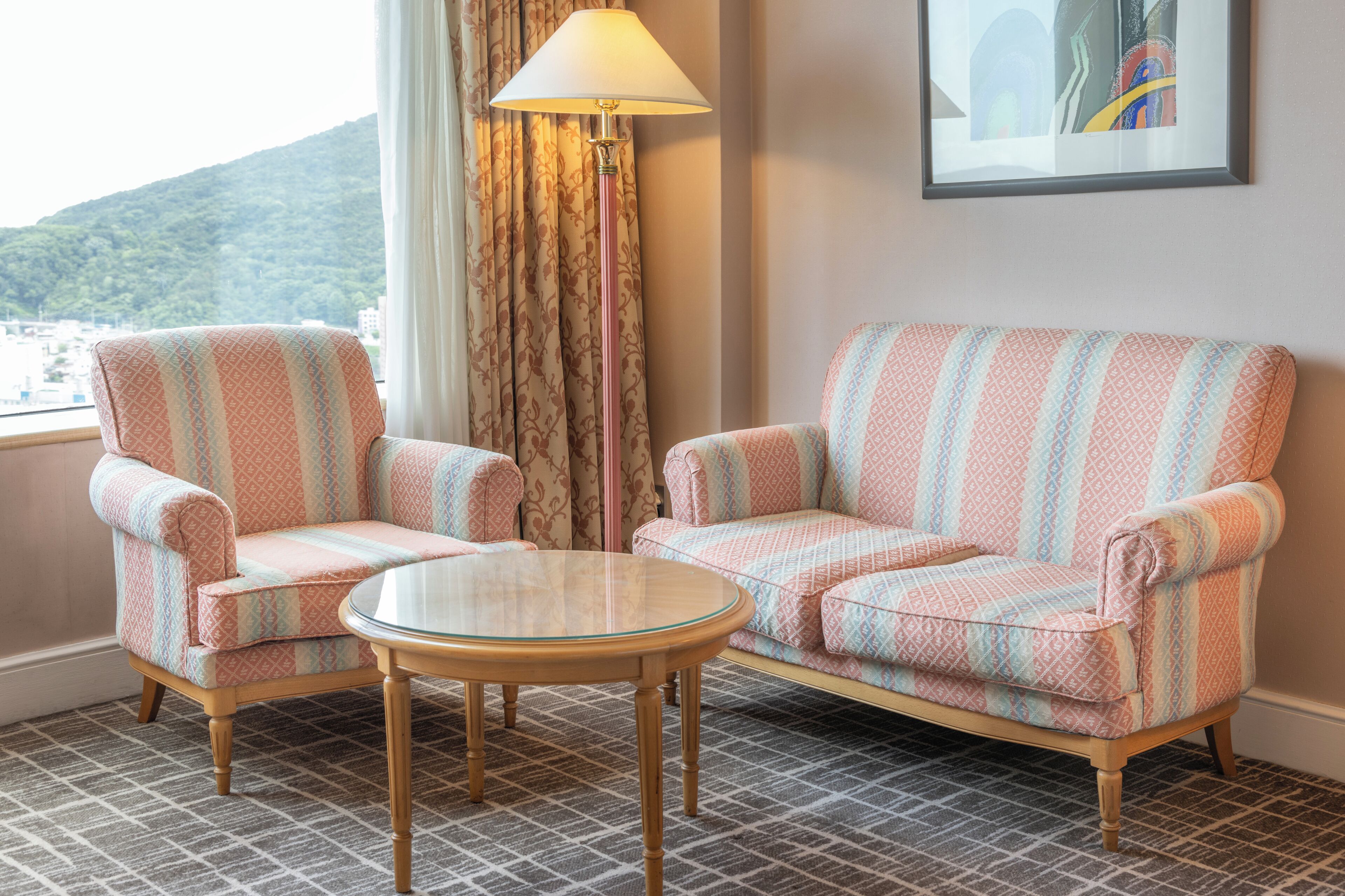 A room with two patterned armchairs, a small round table, and a floor lamp.