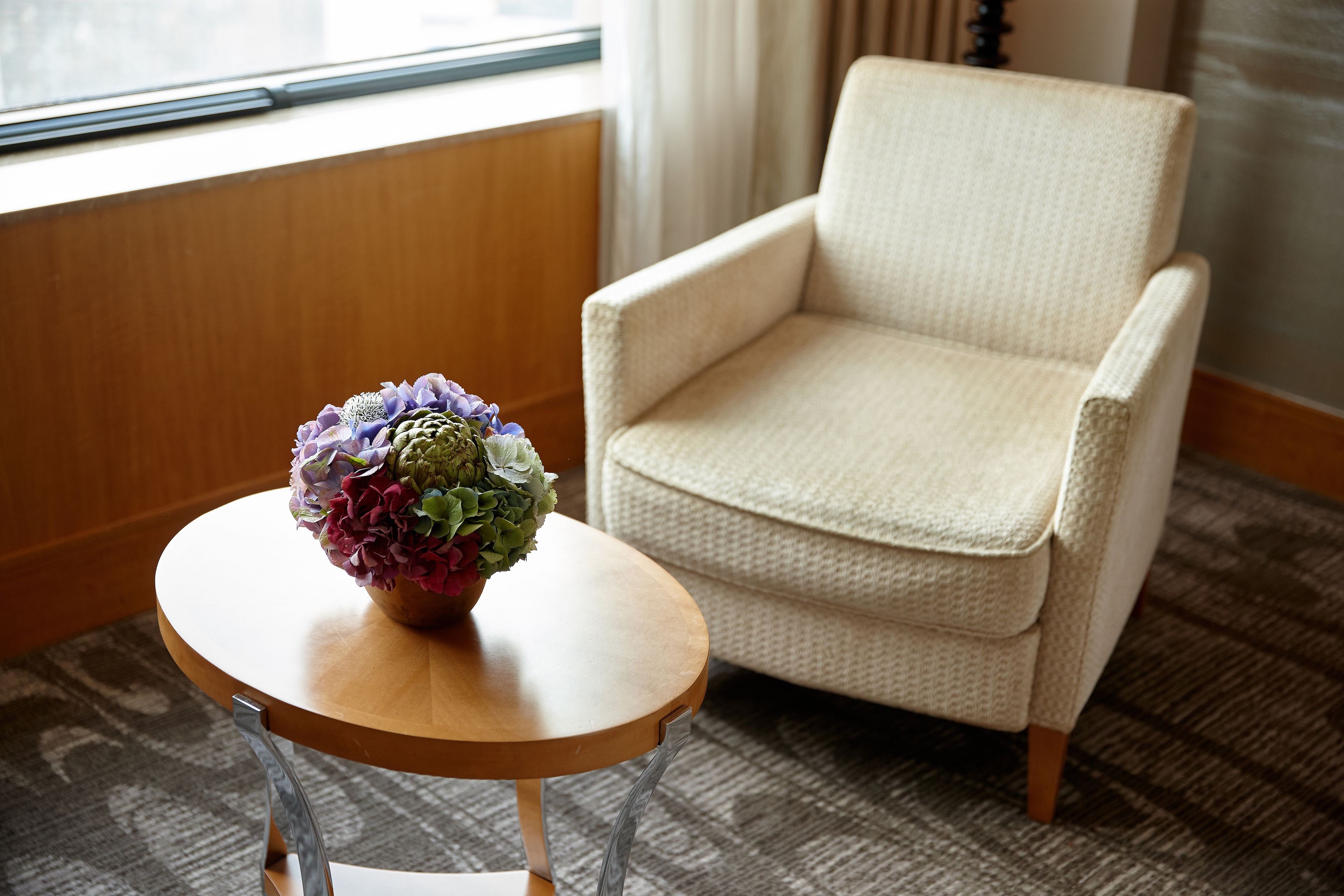 A room with a round wooden table, a beige armchair, and a window with curtains.