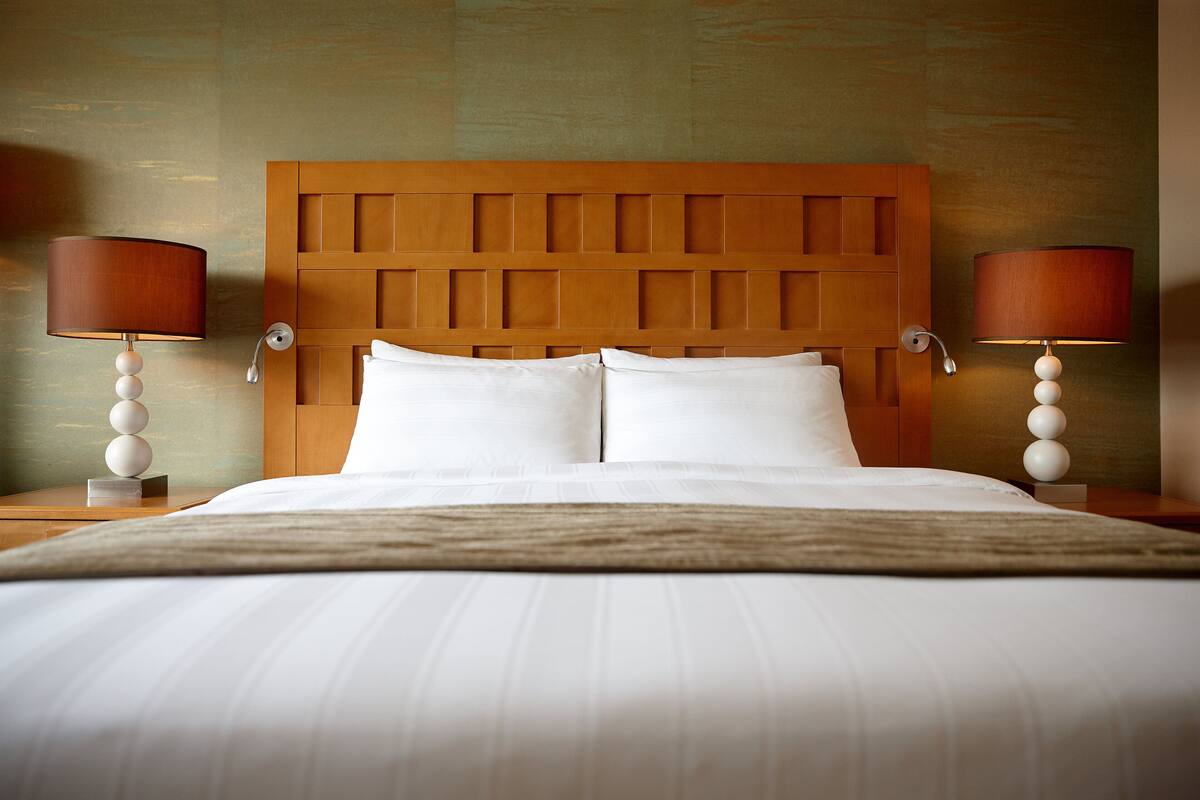 A neatly made bed with a wooden headboard, two bedside lamps, and a fluffy throw blanket.