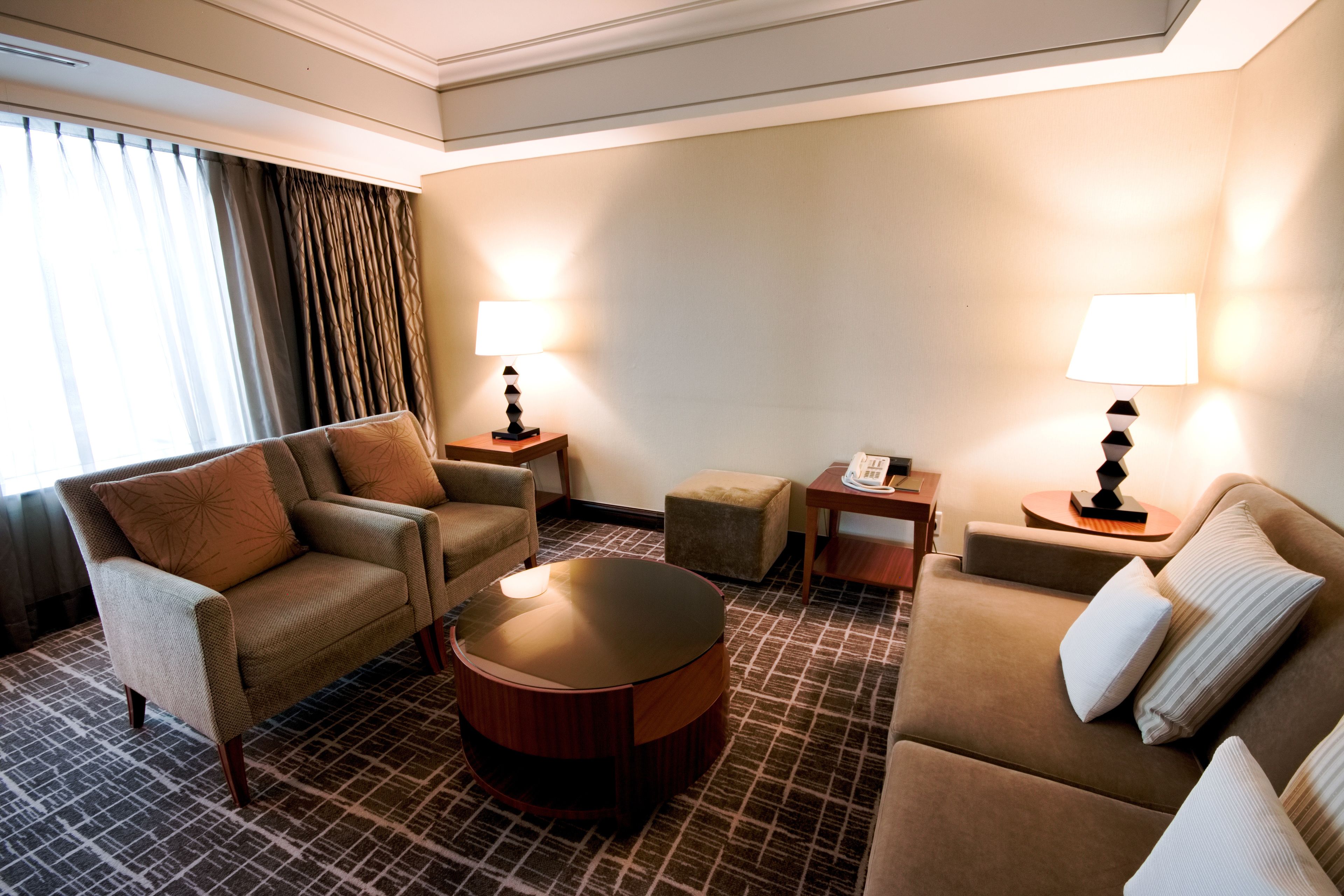 Una habitación de hotel con un sofá, dos sillones, una mesa de centro y dos lámparas.