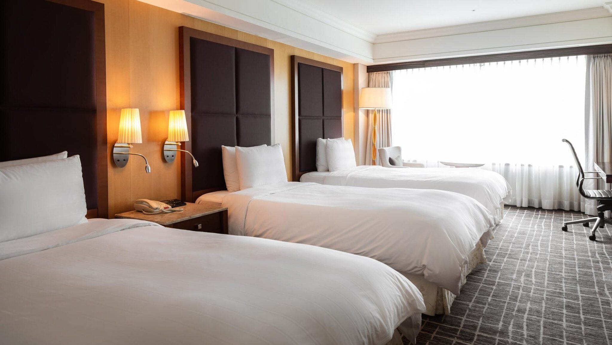 Een hotelkamer met drie bedden, een bureau met telefoon en een stoel.