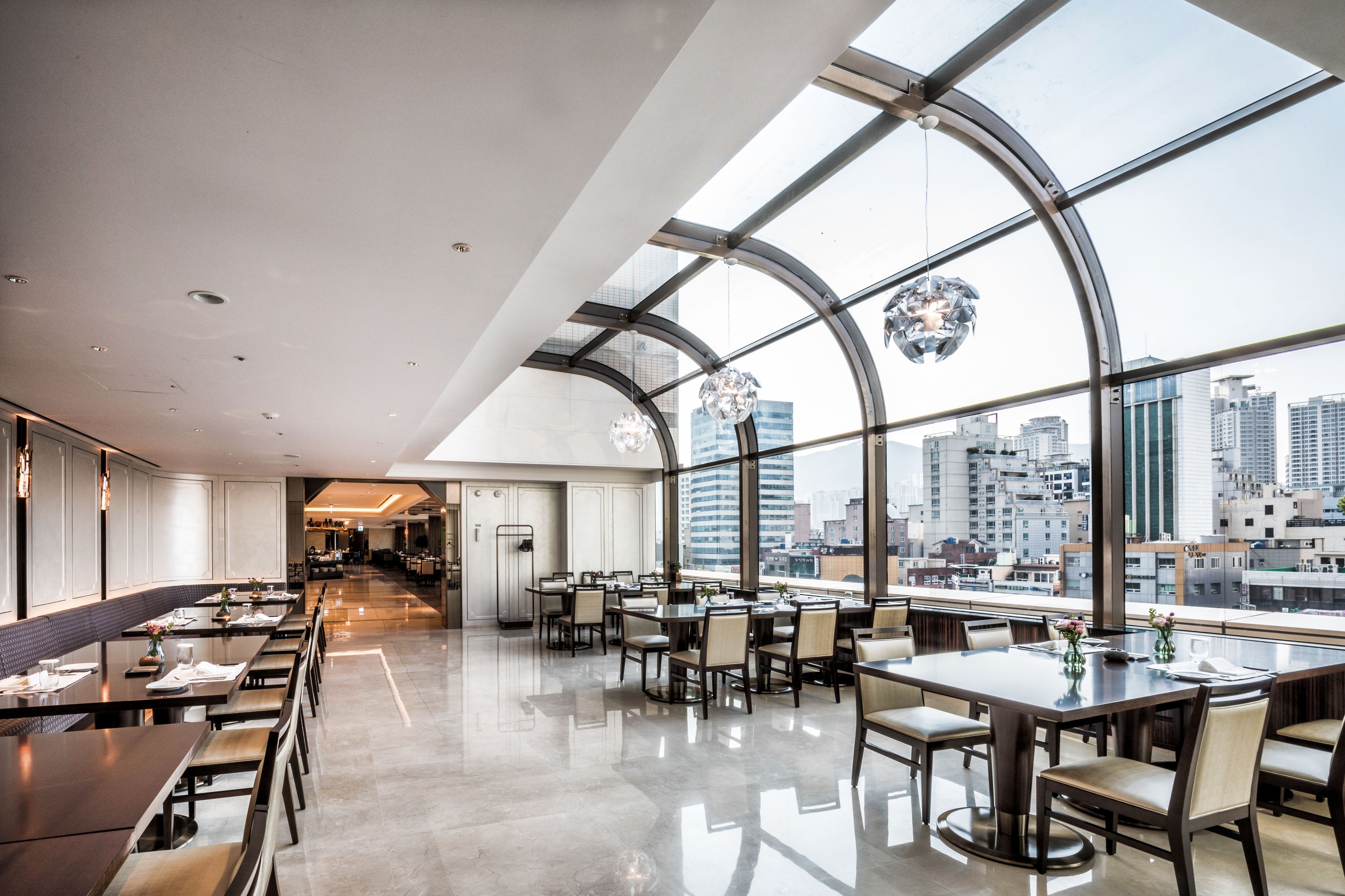 A modern dining area with high ceilings and large windows offering a city view.