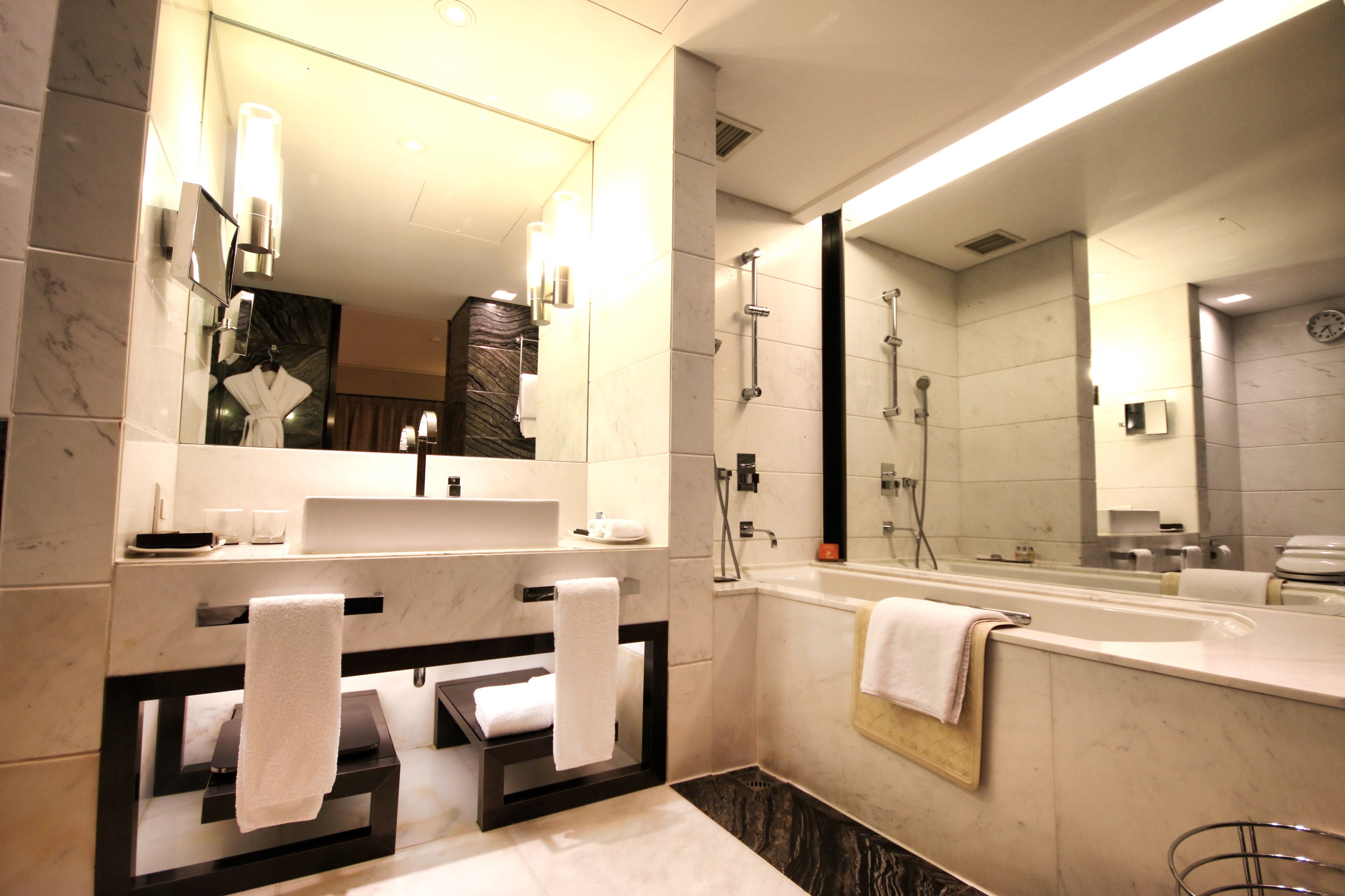A modern bathroom with a large mirror, a bathtub, a shower area, and a vanity with a sink and towel rack.