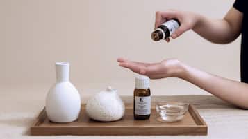 Ein Holztablett mit einer weißen Vase, einem strukturierten Behälter und einer kleinen Flasche mit dem Aufdruck 'Nourishing Laune Capilare DT' auf einem Teppichboden.