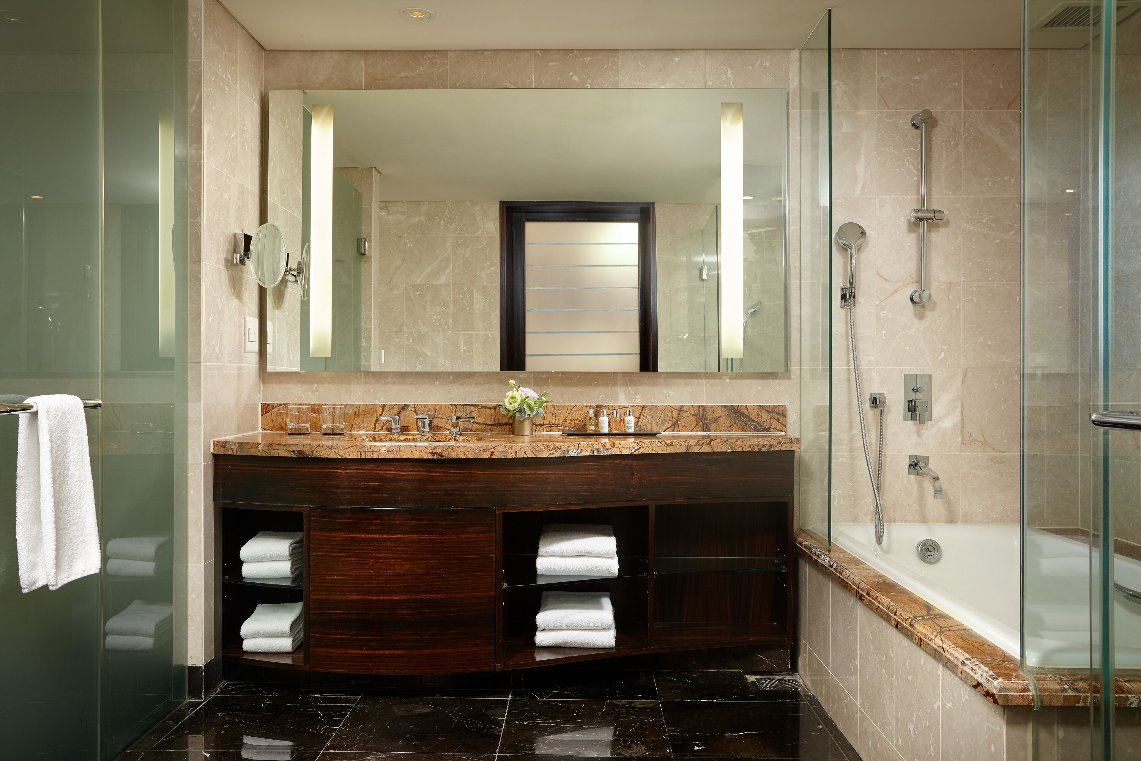 A modern bathroom with a glass-enclosed shower, a large mirror, and a marble countertop.