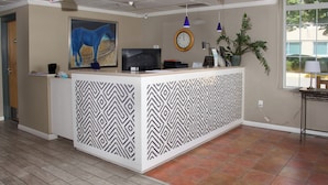 A reception area with a patterned partition, a clock, a television, and a potted plant.