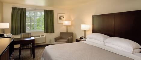 A hotel room with a large bed, a desk, a chair, two bedside lamps, a window with curtains, and a framed picture on the wall.