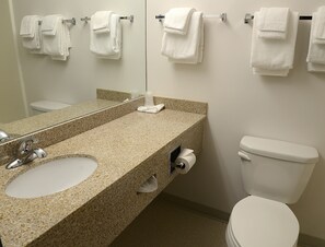 A bathroom with a granite countertop, a sink, a mirror, a toilet, and multiple white towels hanging on a rack.