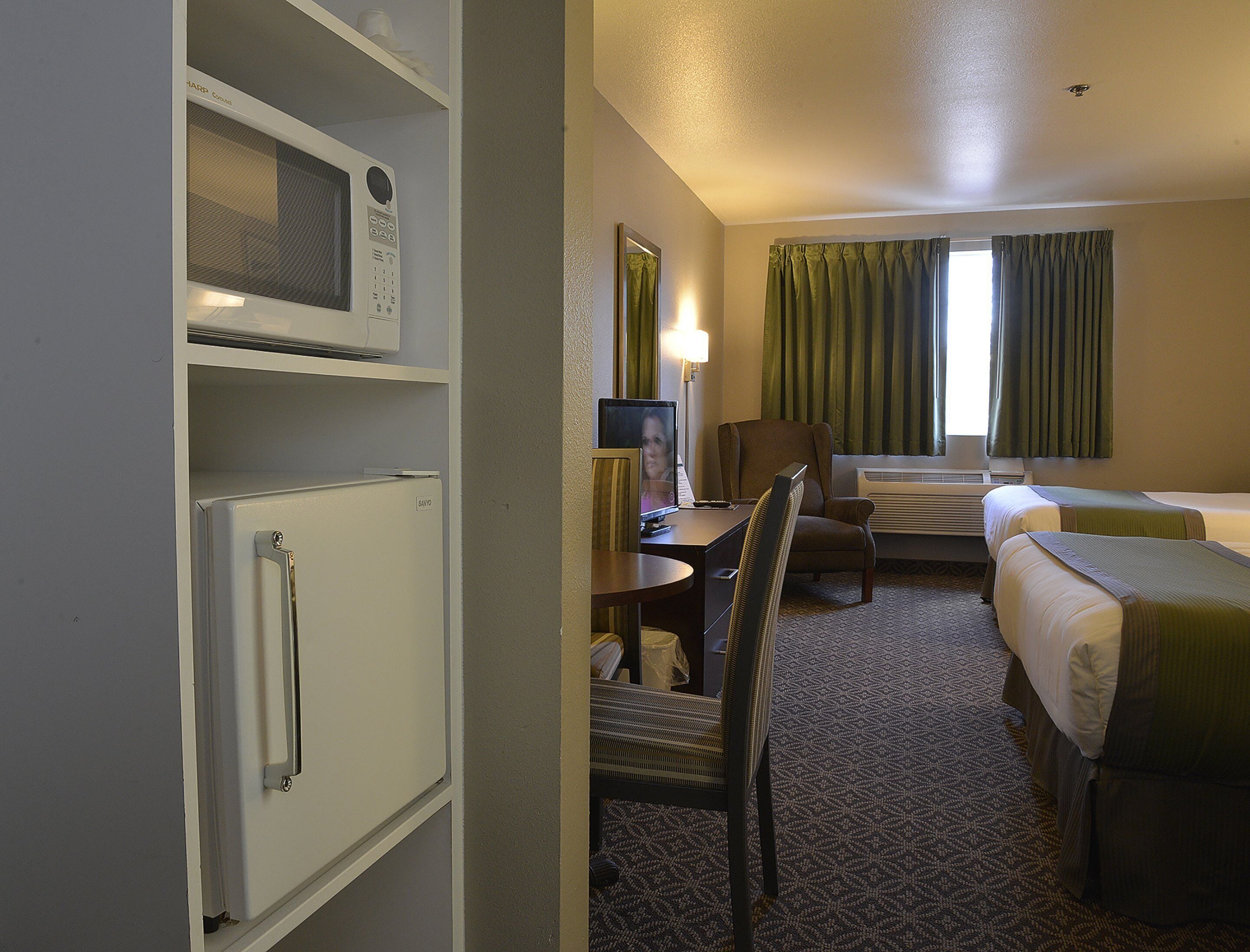 A hotel room with a bed, a desk with a computer, a chair, a microwave, and a small refrigerator.