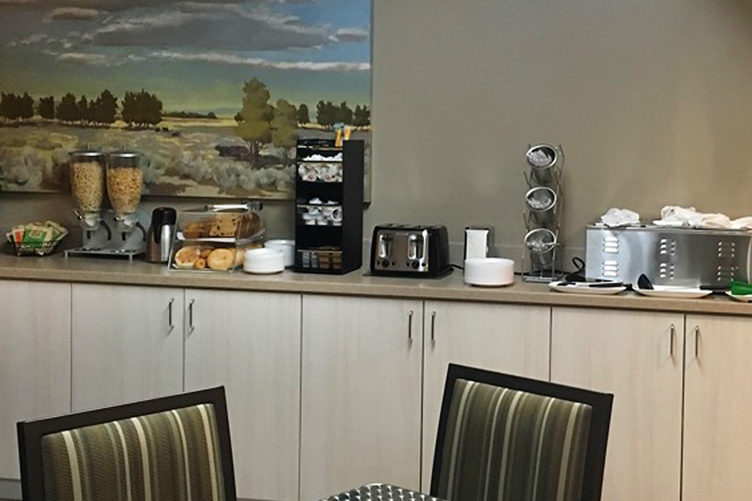 Uma cozinha com um quadro de paisagem, uma cafeteira, uma torradeira e um armário com gavetas.