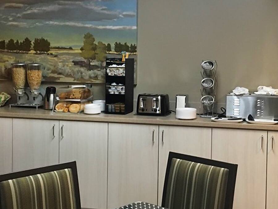 Uma cozinha com um quadro de paisagem, uma cafeteira, uma torradeira e um armário com gavetas.
