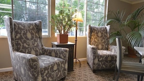 A room with two patterned armchairs, a small table with a lamp, and a potted plant.