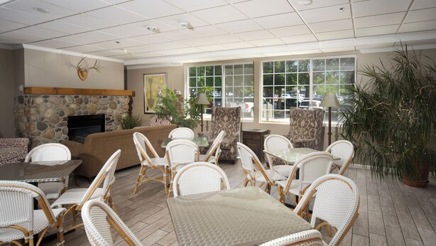 A spacious indoor area with a stone fireplace, wicker furniture, and large windows offering a view of parked cars outside.