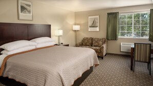 A hotel room with a large bed, a chair, a desk, and a window with curtains.