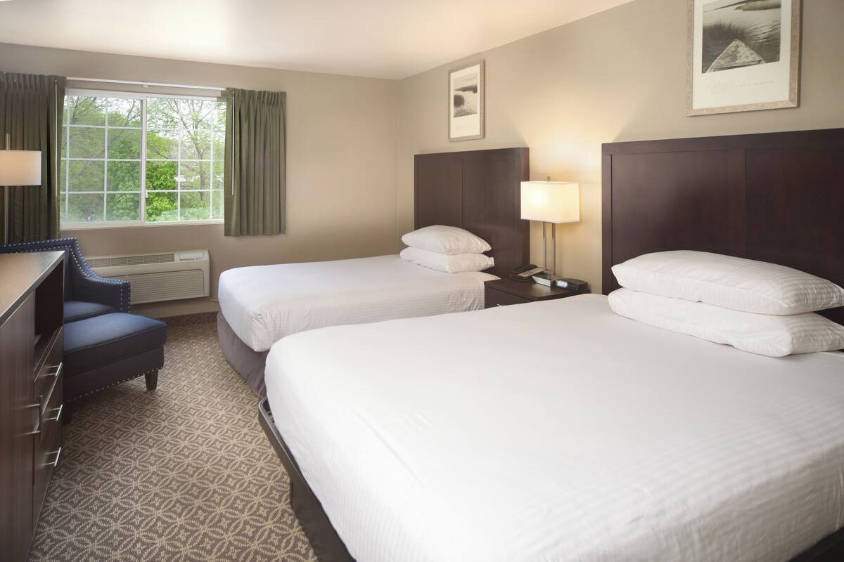 A hotel room with two beds, a desk, a chair, and a window with curtains.