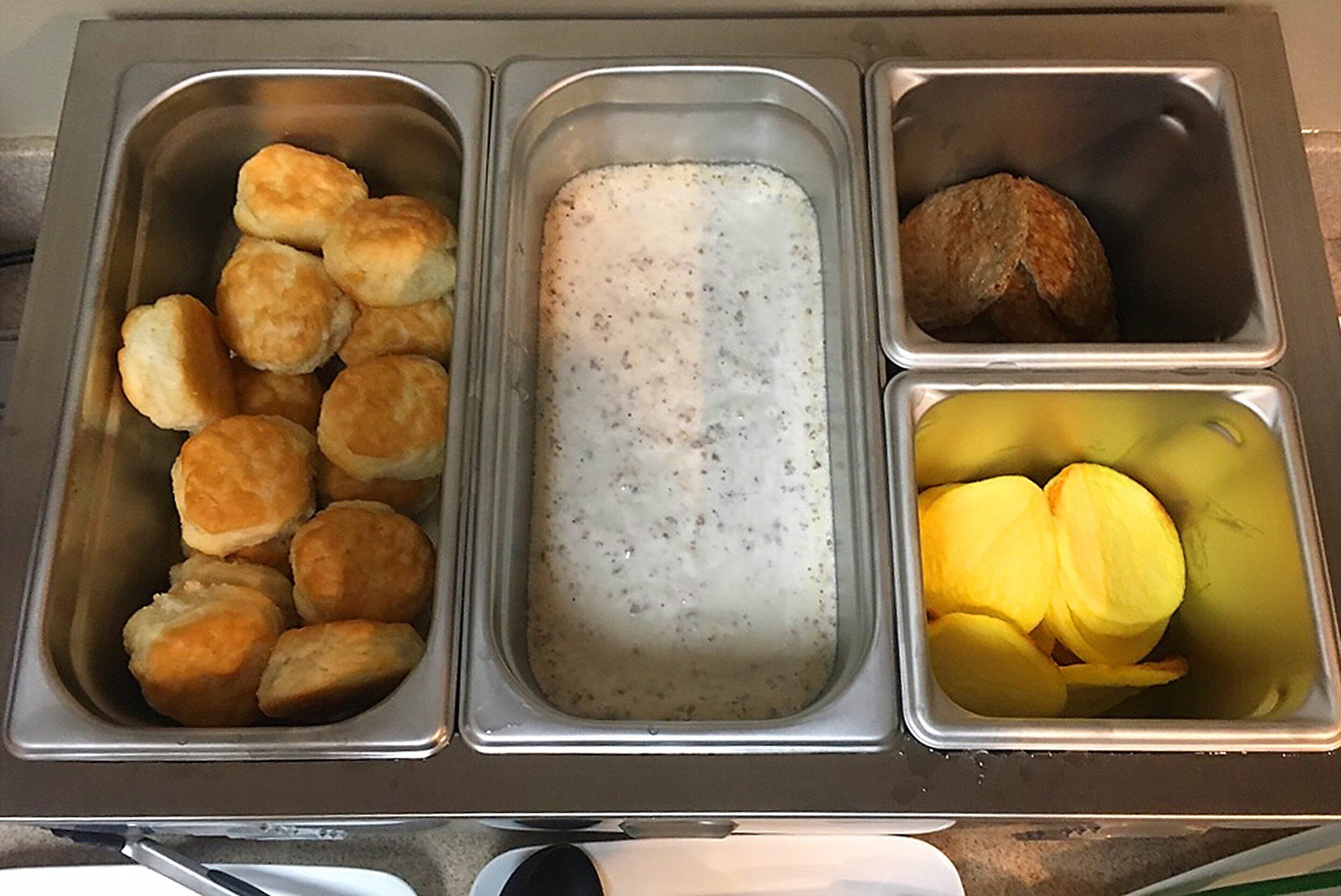 A stainless steel food service station with compartments containing biscuits, a creamy beverage, and sliced apples.