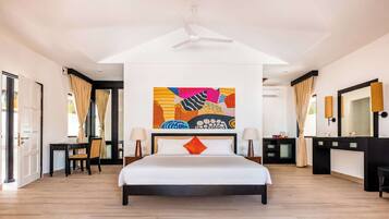 Um quarto espaçoso com uma cama grande, um ventilador de teto, um quadro abstrato colorido e um banheiro moderno com um espelho grande e um lavatório preto.