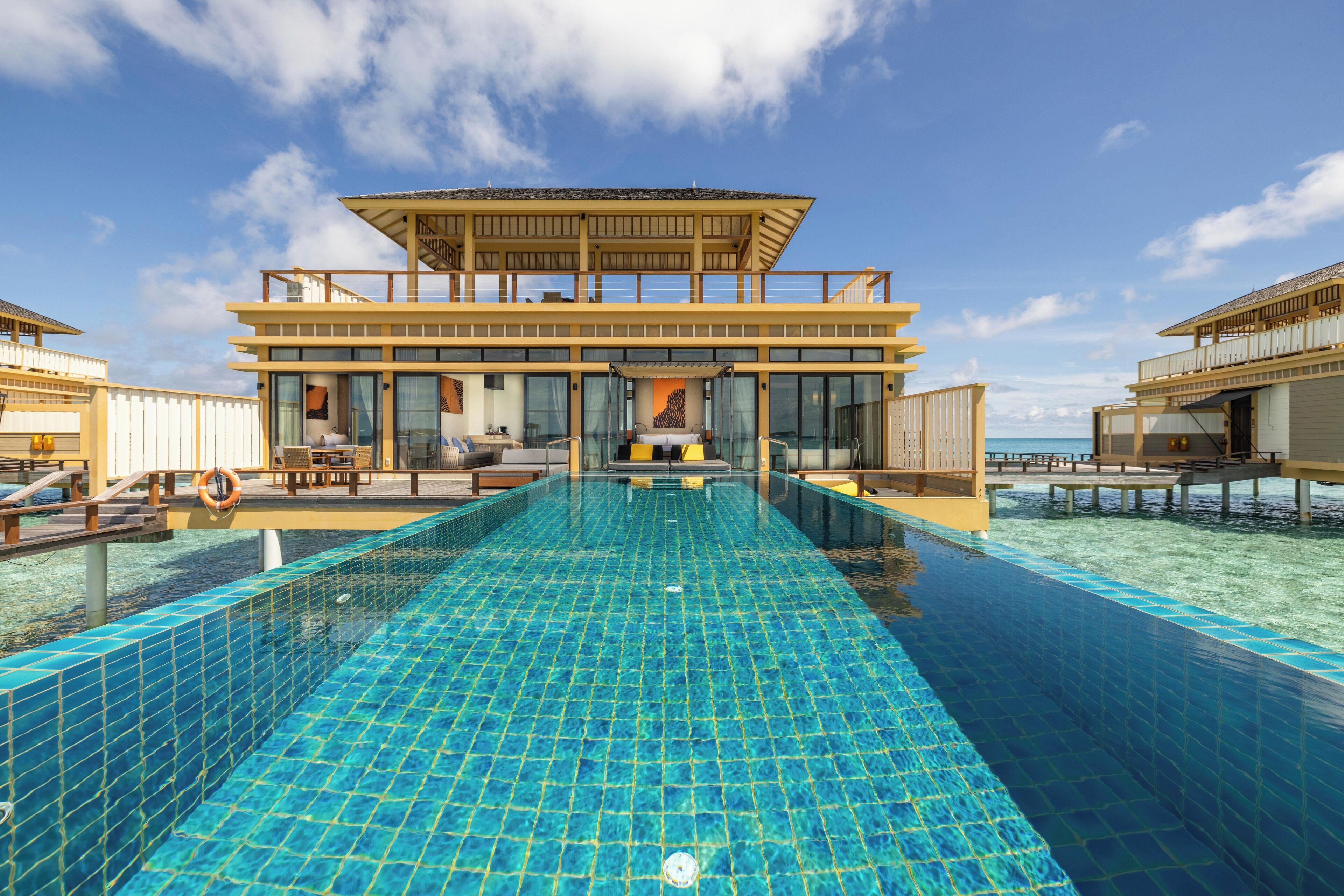 A resort with a large infinity pool, overwater bungalows, and a clear view of the ocean.