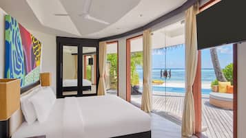 Habitación de hotel moderna con una cama grande, un ventilador de techo y vista al océano a través de puertas correderas amplias.