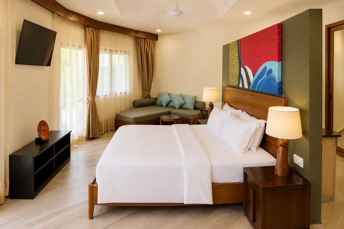 A hotel room with a large bed, a sofa, a TV, and a painting on the wall.
