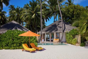 A beachside resort with thatched-roof huts, a pool, and sun loungers.