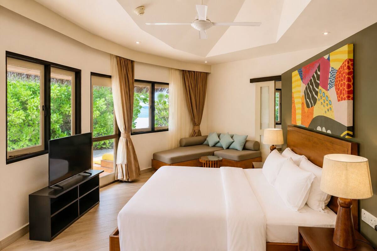 A hotel room with a bed, a sofa, a TV, and a painting on the wall.