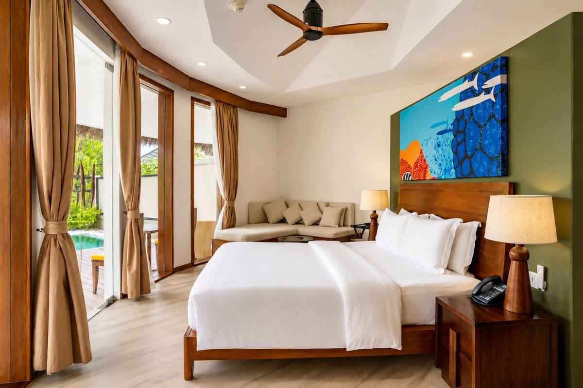 A hotel room with a large bed, a sofa, a ceiling fan, and a painting on the wall.