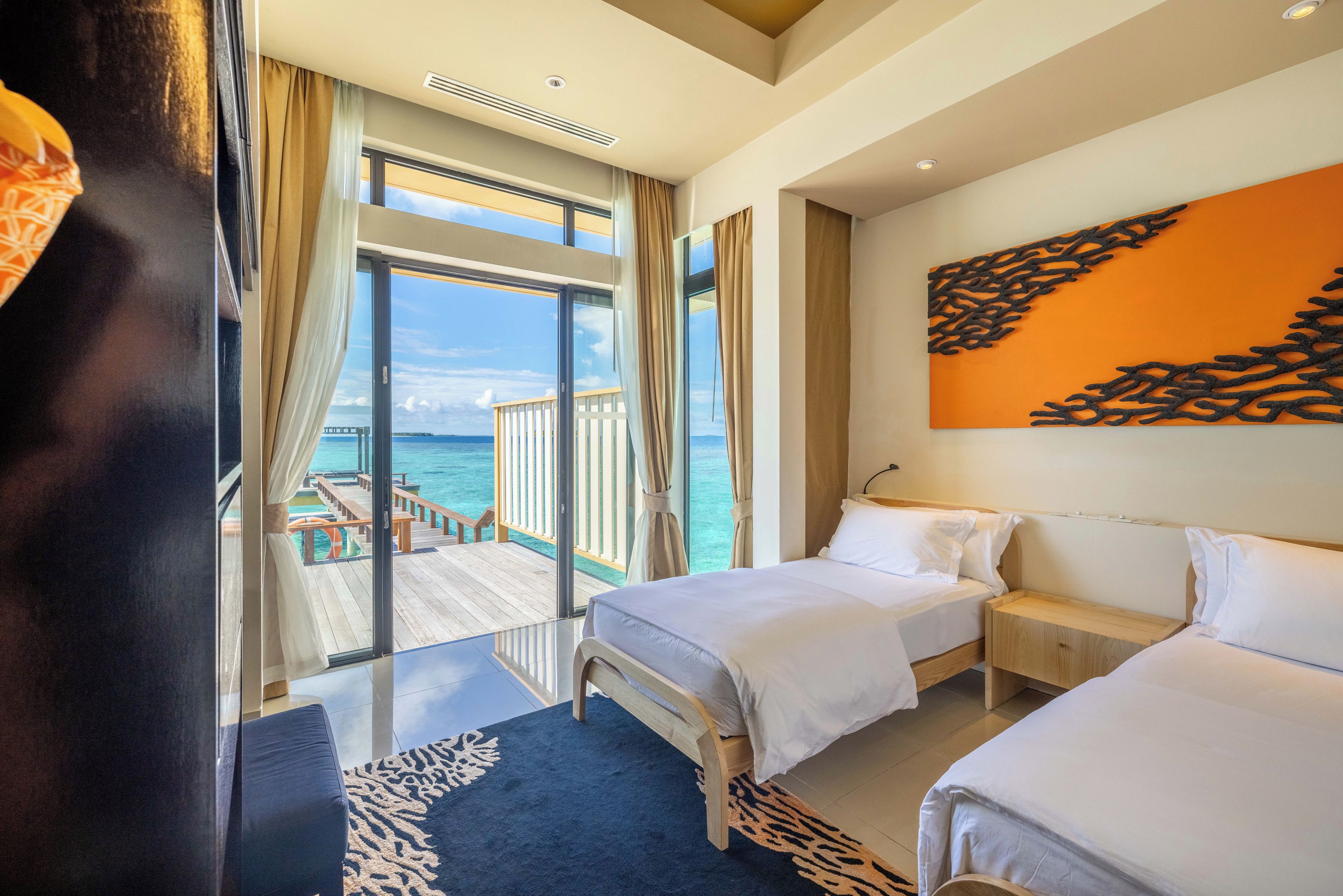 Habitación de hotel con dos camas, un ventanal con vistas al mar y un balcón con terraza de madera.