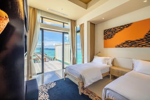 Une chambre d’hôtel avec deux lits, une grande fenêtre donnant sur la mer et un balcon avec une terrasse en bois.