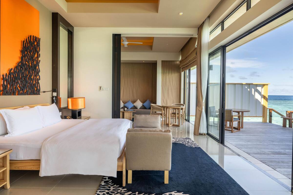 A modern hotel room with a large bed, a seating area, and a view of the ocean.