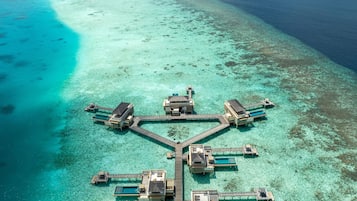 An overwater bungalows connected by a wooden walkway, surrounded by clear turquoise waters and a small island.