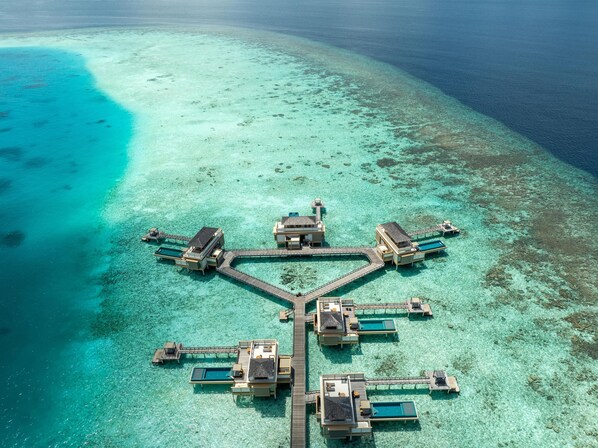 An overwater bungalows connected by a wooden walkway, surrounded by clear turquoise waters and a small island. - Angsana Velavaru - Free return Seaplane Transfers (Velavaru)