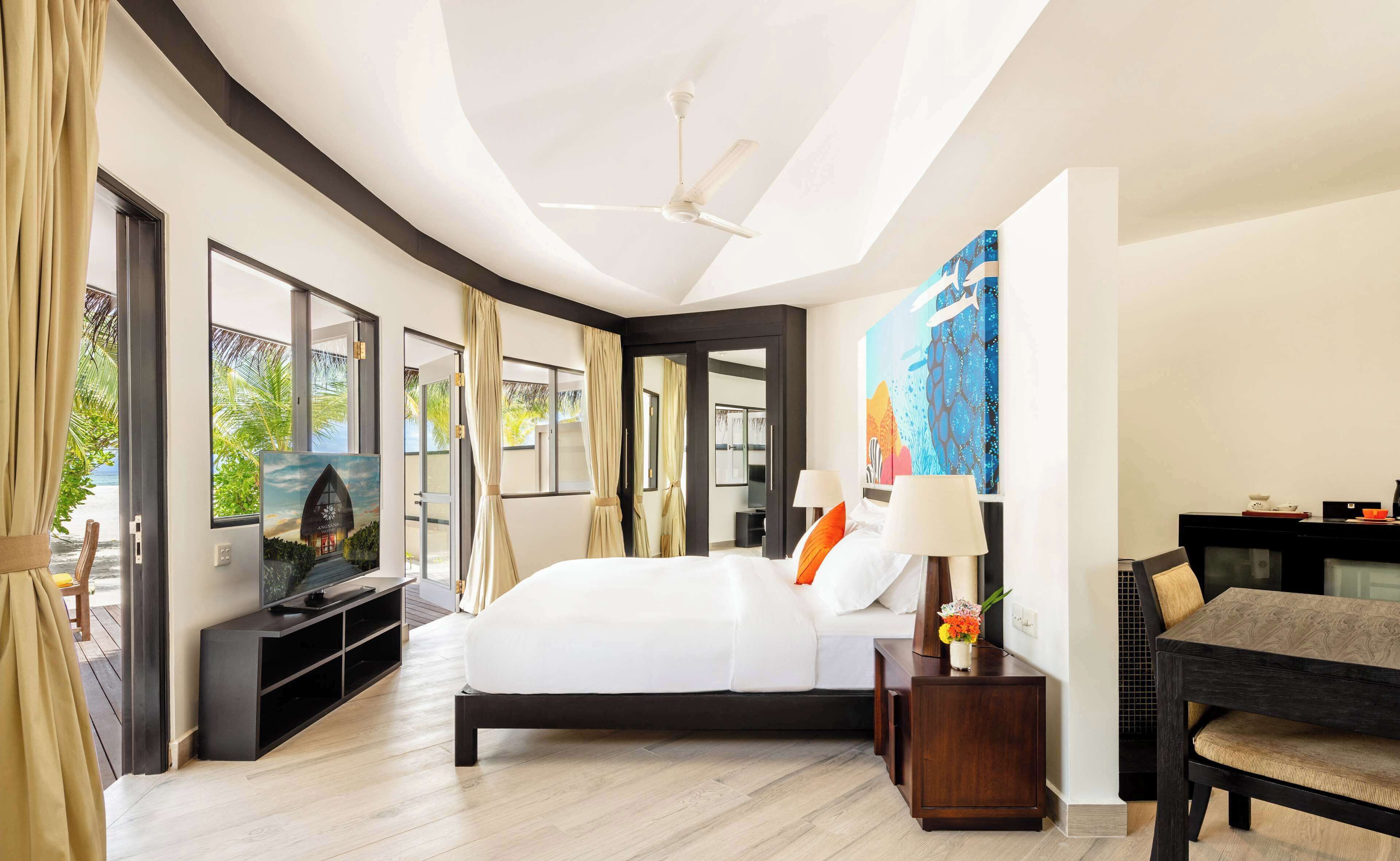 A modern hotel room with a large bed, a flat-screen TV, a desk with a chair, and a ceiling fan.