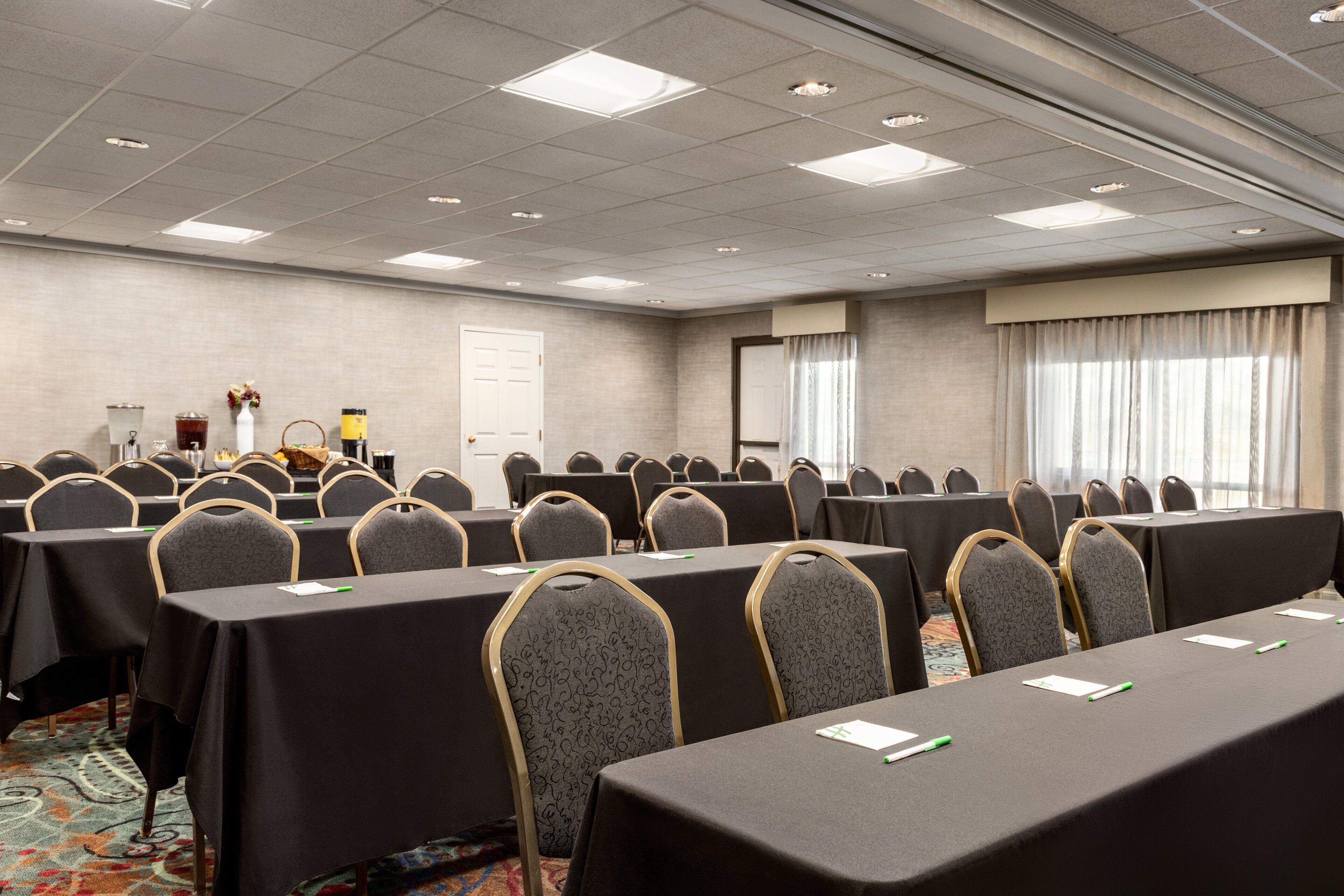 A conference room with rows of tables and chairs, a door, and a window with curtains.