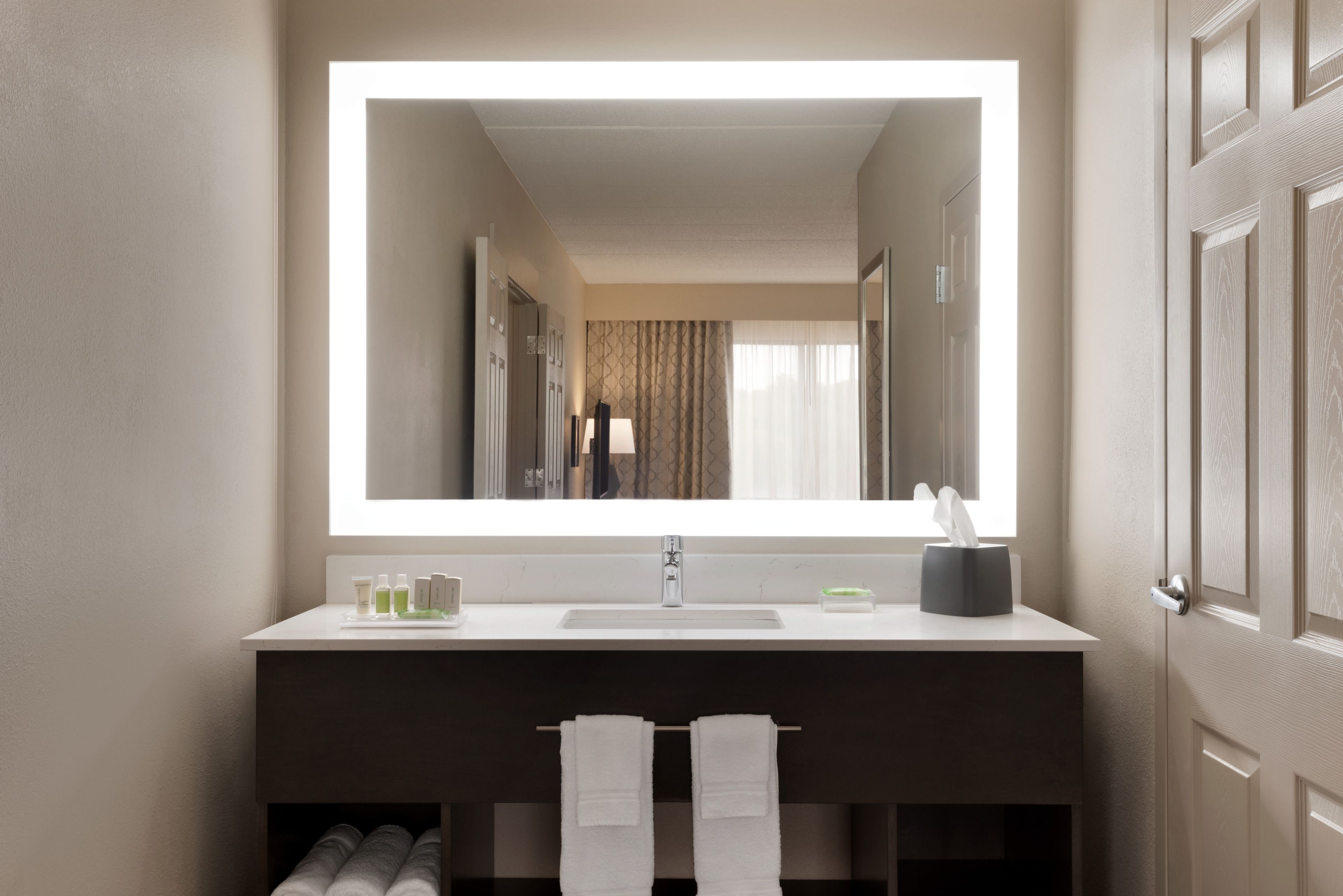 A modern bathroom with a large mirror, a sink, and towel racks.
