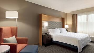 Une chambre d’hôtel avec un lit, un bureau, une chaise, une lampe et une fenêtre avec des rideaux.