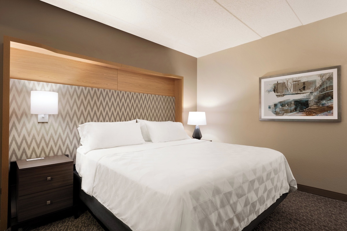 A hotel room with a bed, two bedside tables, a wall-mounted lamp, and a framed picture.
