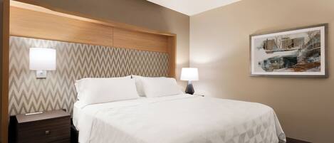 A hotel room with a bed, nightstand, lamps, and a framed picture on the wall.