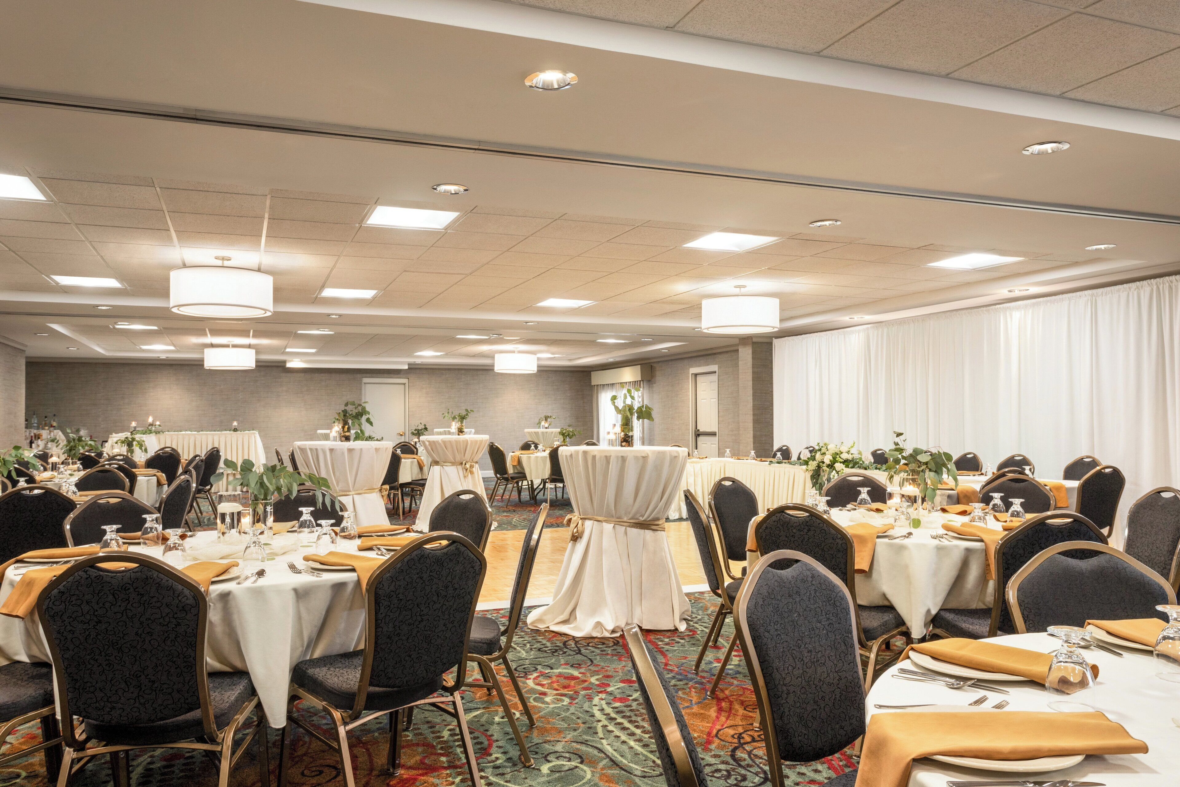 A banquet hall with round tables, chairs, and a carpeted floor.