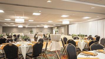 A banquet hall with round tables, chairs, and a carpeted floor.