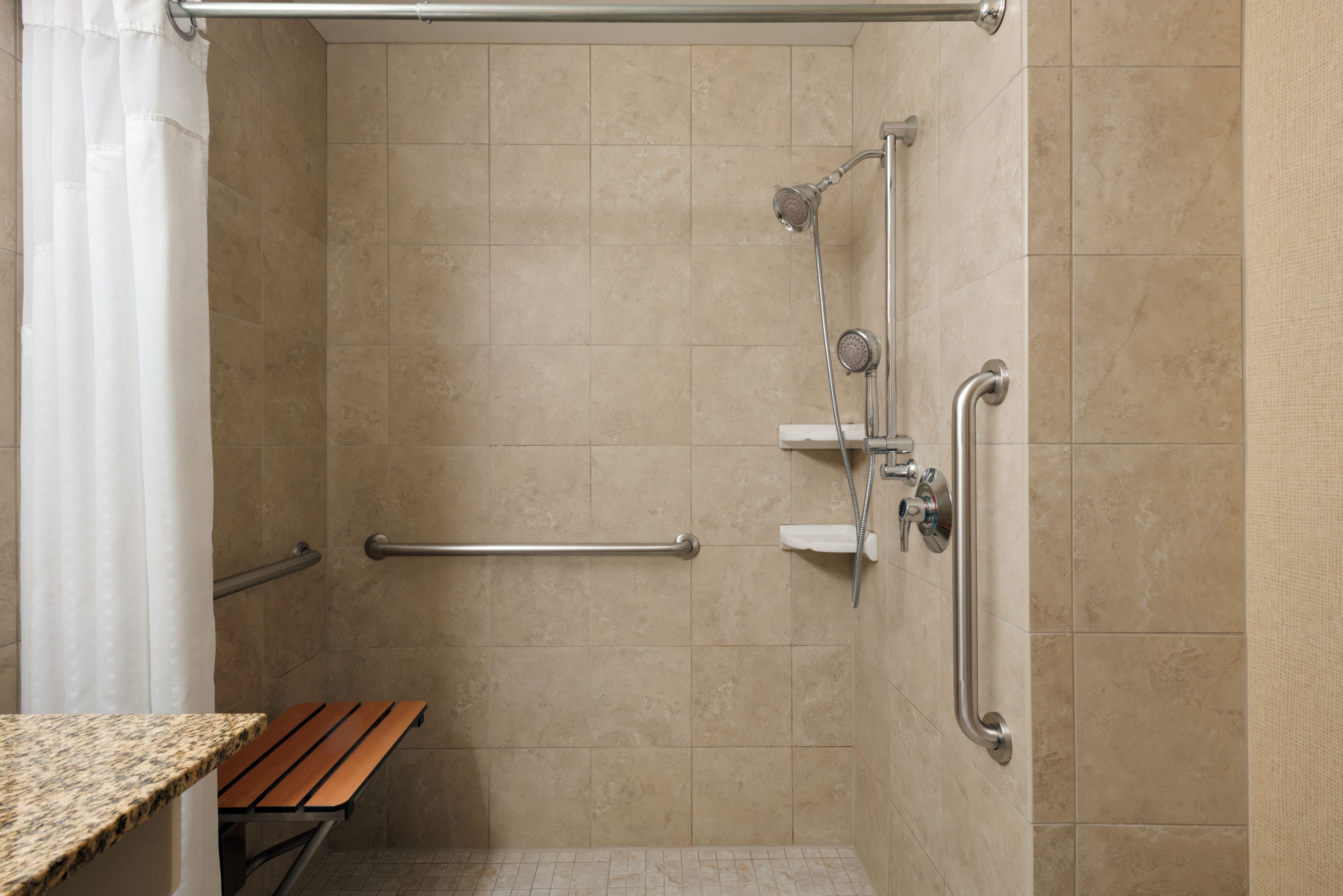 A shower area with beige tiles, a grab bar, a bench, and a showerhead.