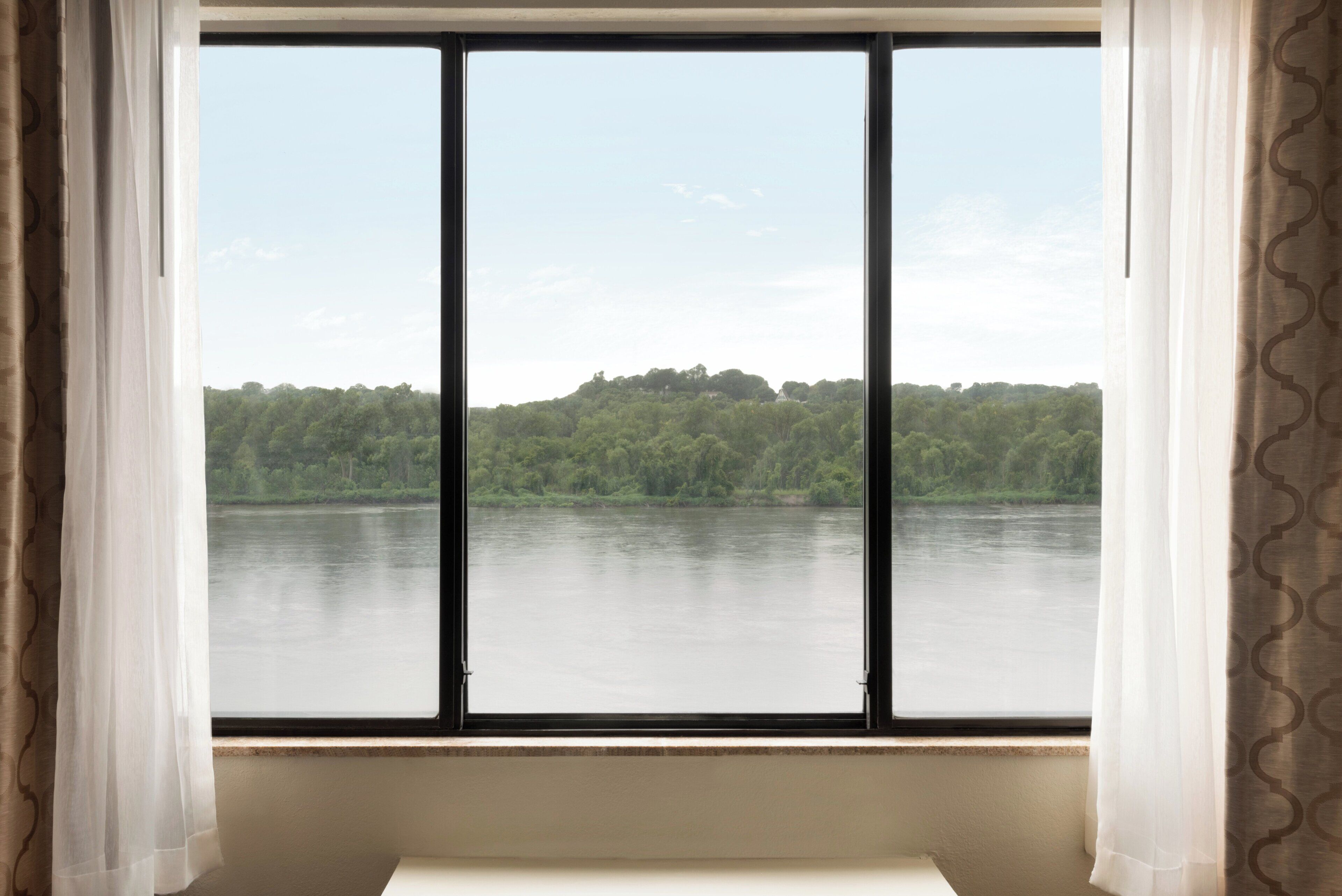 A room with a large window overlooking a body of water and a forested area.