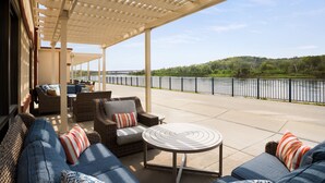 An outdoor patio with wicker furniture, a round table, and a view of a river.