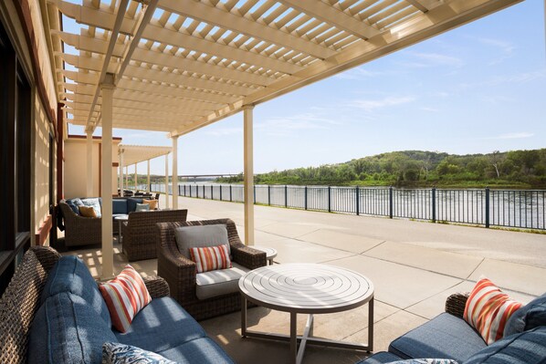 An outdoor patio with wicker furniture, a round table, and a view of a river. - Holiday Inn Hotel & Suites Council Bluffs I-29 by IHG (Council Bluffs)
