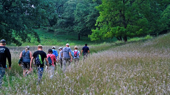 A group of people hiking in a grassy area with trees in the background. - Holiday Inn Hotel & Suites Council Bluffs I-29 by IHG (Council Bluffs)