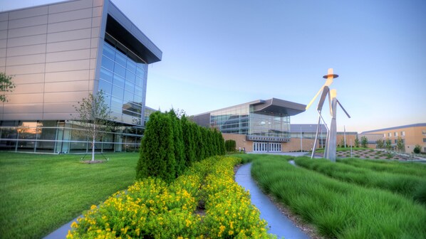 A modern building with a glass facade, a landscaped garden with yellow flowers, and a distinctive sculpture. - Holiday Inn Hotel & Suites Council Bluffs I-29 by IHG (Council Bluffs)