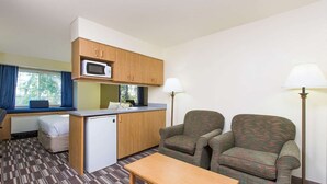 A compact room with a kitchenette, two armchairs, a small table, and a window with curtains. - Baymont Inn & Suites by Wyndham Anchorage Airport (Anchorage)