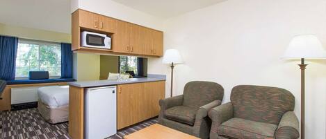 Una habitación pequeña con kitchenette, dos sillones, una mesita y una ventana con cortinas.