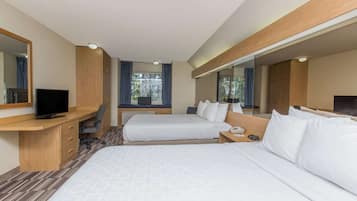 A hotel room with two beds, a desk with a TV, a large mirror, and a window with curtains.