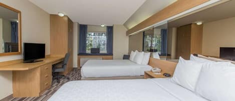 A hotel room with two beds, a desk with a TV, a large mirror, and a window with curtains.